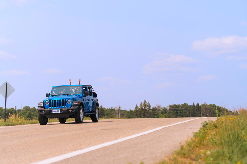 Blue jeep with girls driving down road.