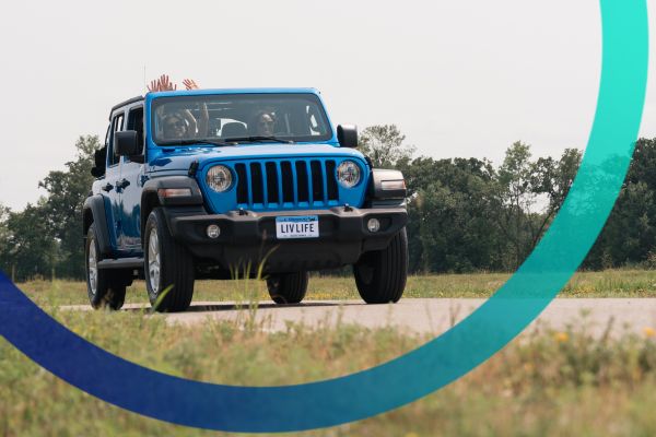 Blue jeep driving on a country road with young women laughing.